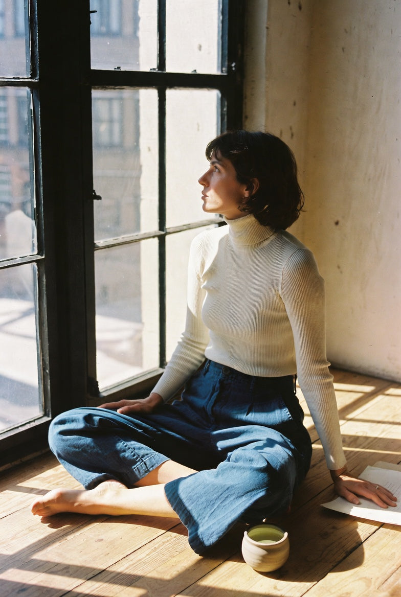 Woman in ivory turtleneck sitting cross-legged by a sunlit window, North Node in Aquarius 2026 rising sign guide