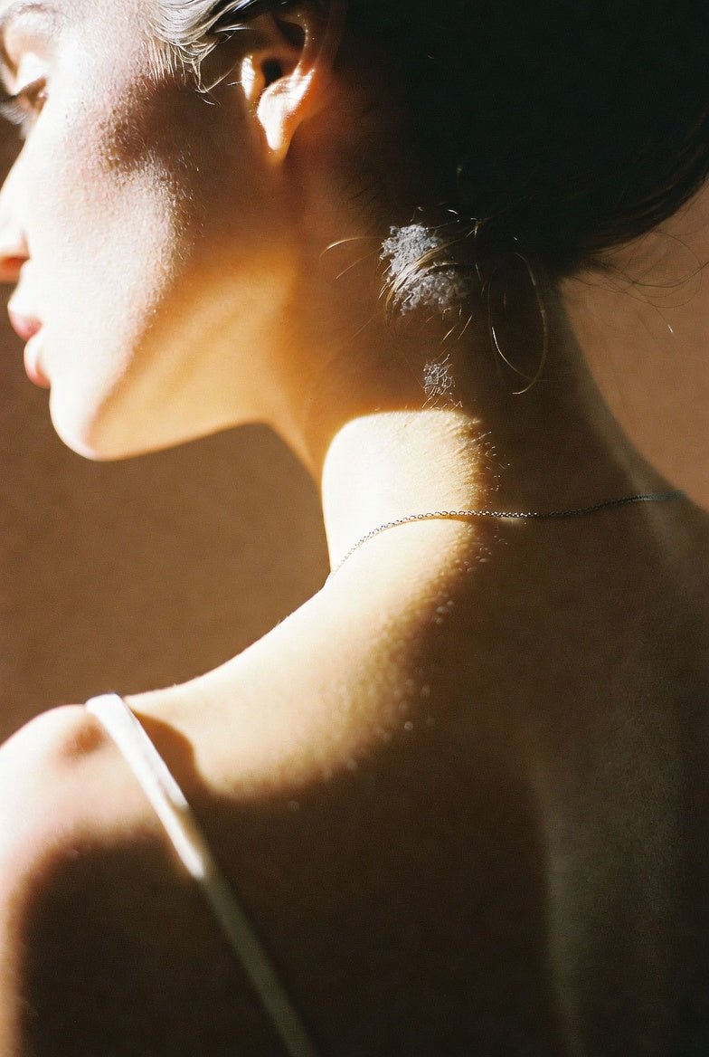 Warm sunlight on the back of a woman's neck and shoulder, delicate silver chain, silk strap, quiet editorial portrait for thewuwu weekly cosmic forecast.