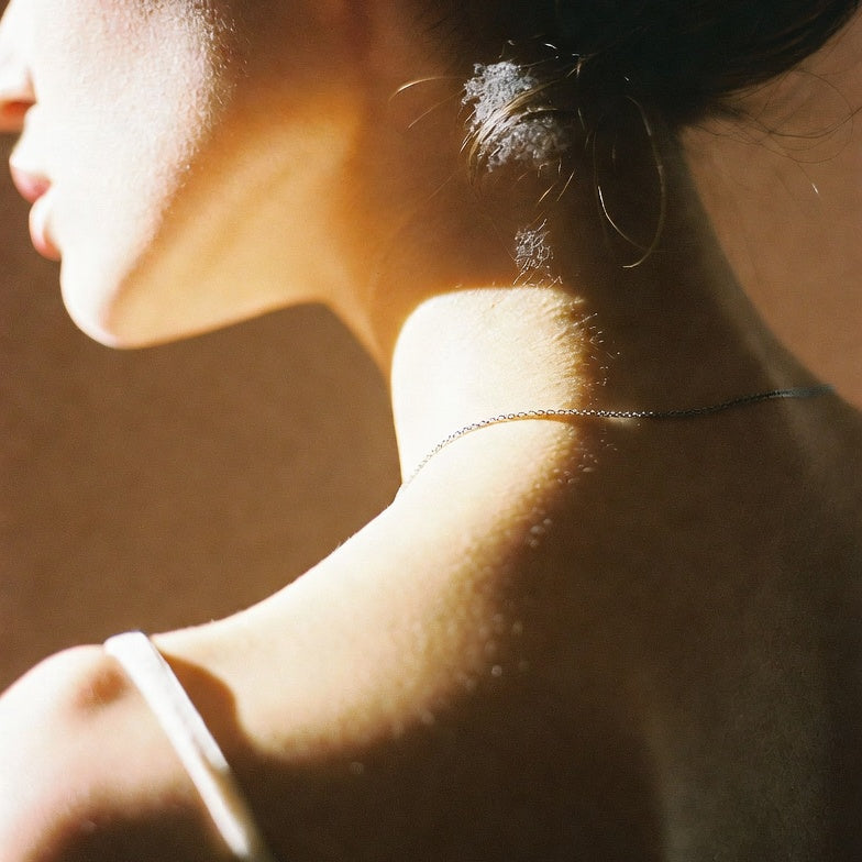 Warm sunlight on the back of a woman's neck and shoulder, delicate silver chain, silk strap, quiet editorial portrait for thewuwu weekly cosmic forecast.