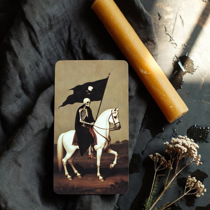 The Death tarot card face up on rumpled dark linen beside a hand-poured amber beeswax candle and a sprig of dried yarrow, soft window light on wet stone