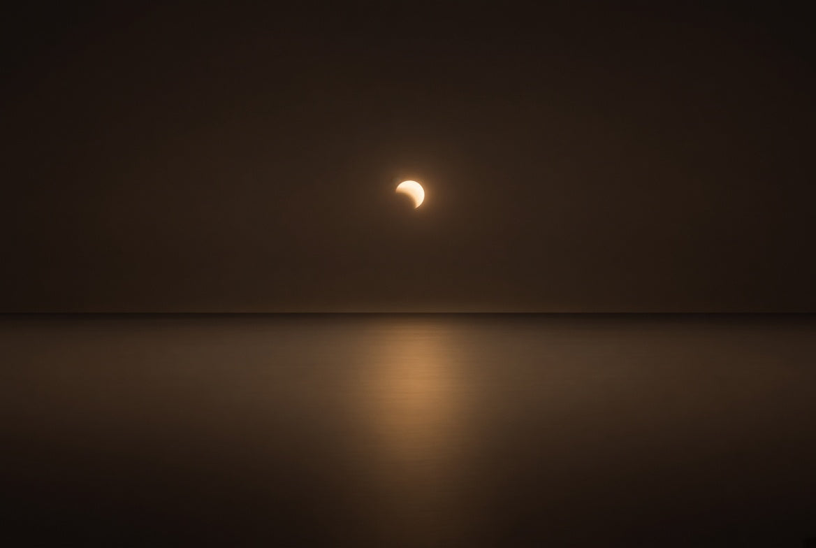 Partial lunar eclipse rising in warm amber light over a calm still ocean at night, symbolizing the Pisces lunar eclipse of August 28, 2026.