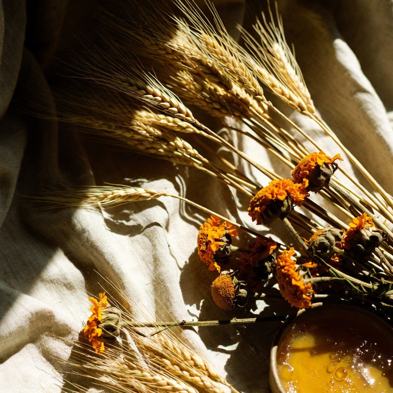 Sun-warmed golden wheat and dried marigold arranged on rumpled oat linen beside a small vessel of honey, late-afternoon light